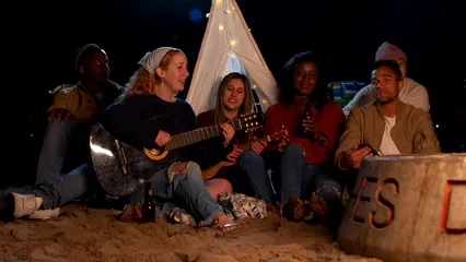 Horizontal video: Group of friends sitting on beach sand playing guitar and singing together 7148257. Duration: 25 seconds. Resolution: 3840x2160