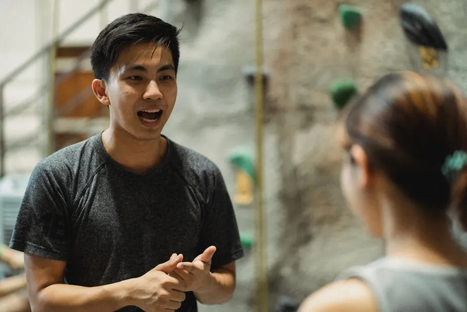 Young ethnic male instructor conversing with crop anonymous mountaineer near climbing wall before practice