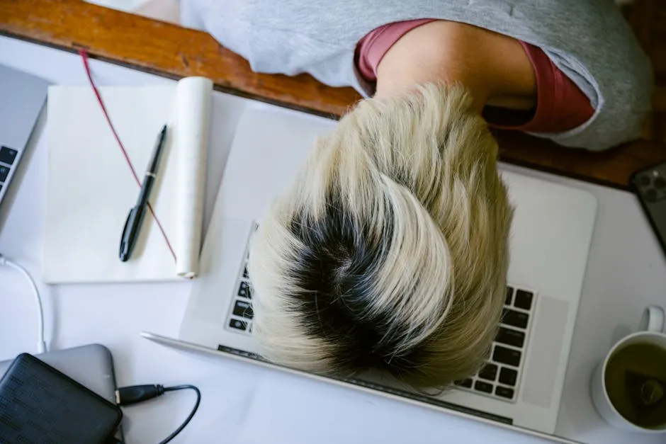 From above of tired fatigued unrecognizable female in casual wear resting head on netbook keyboard near notebook and cup of tea after long working day