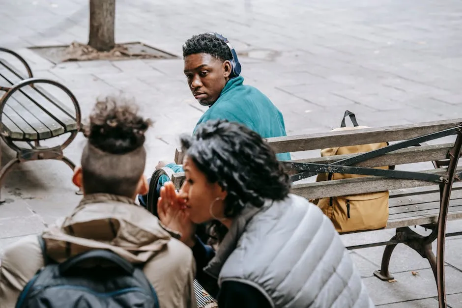 Back view of faceless classmates spreading gossip about African American man on wooden bench