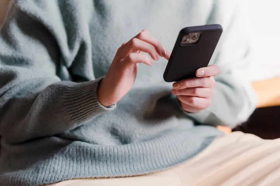 Crop faceless female in casual clothes using smartphone and touching screen while chilling at home