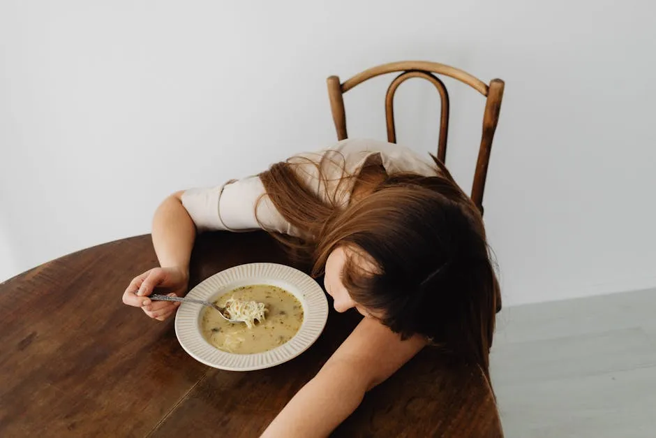 A woman leaning on a table with a bowl of soup, expressing a tired mood.