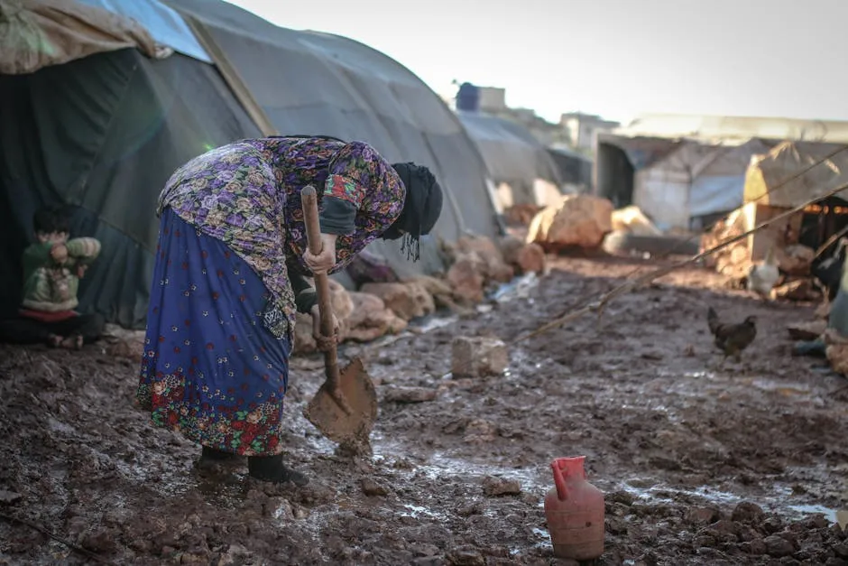 An elderly woman works in the mud at an outdoor refugee camp in Idlib, Syria.