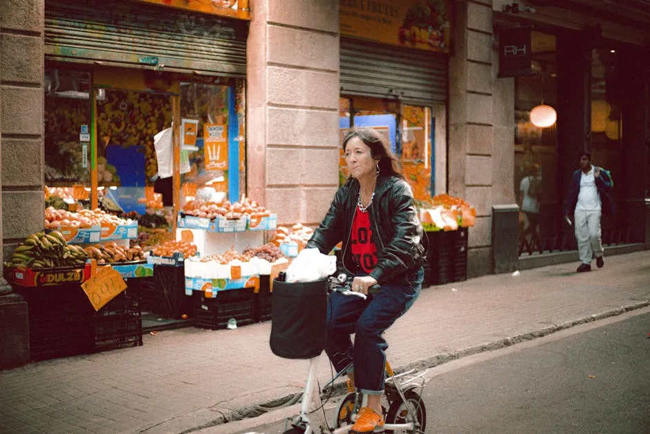 Woman riding a bicycle on a street next to a lively fruit market.