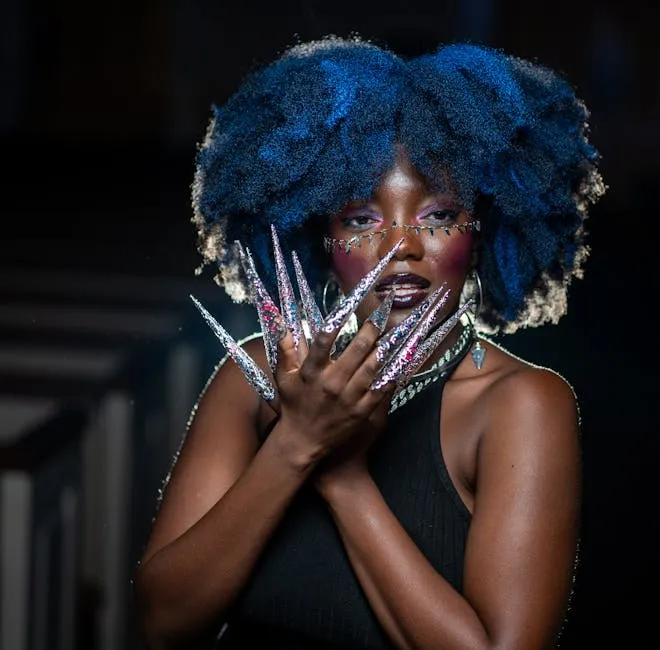 Striking portrait of a woman showcasing vibrant blue hair and elaborate artistic nail art.