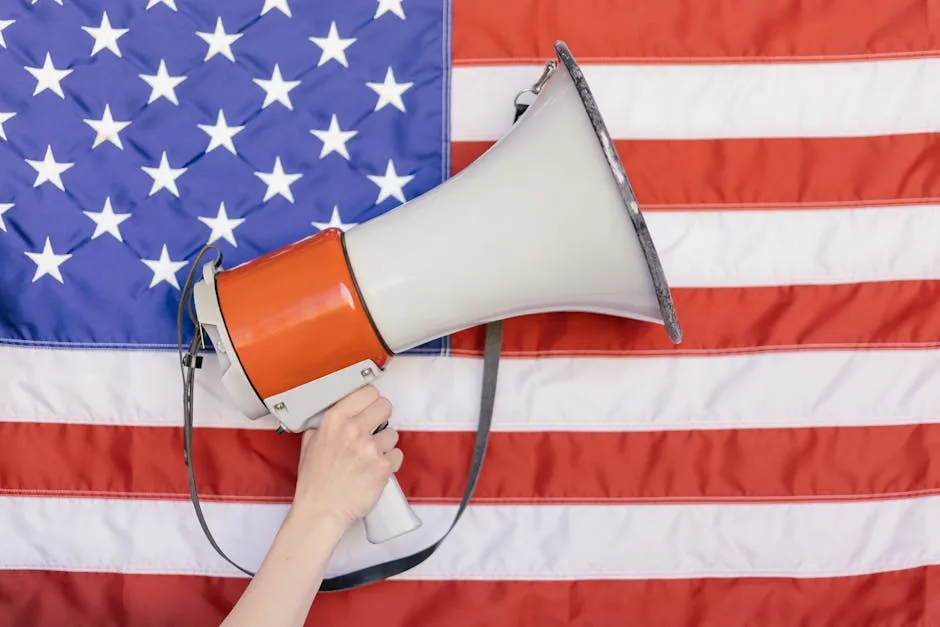 Close-up of a hand holding a megaphone against the backdrop of an American flag, symbolizing freedom of speech.