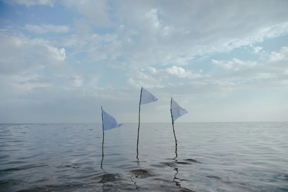 Three white flags on a serene sea under a cloudy sky.