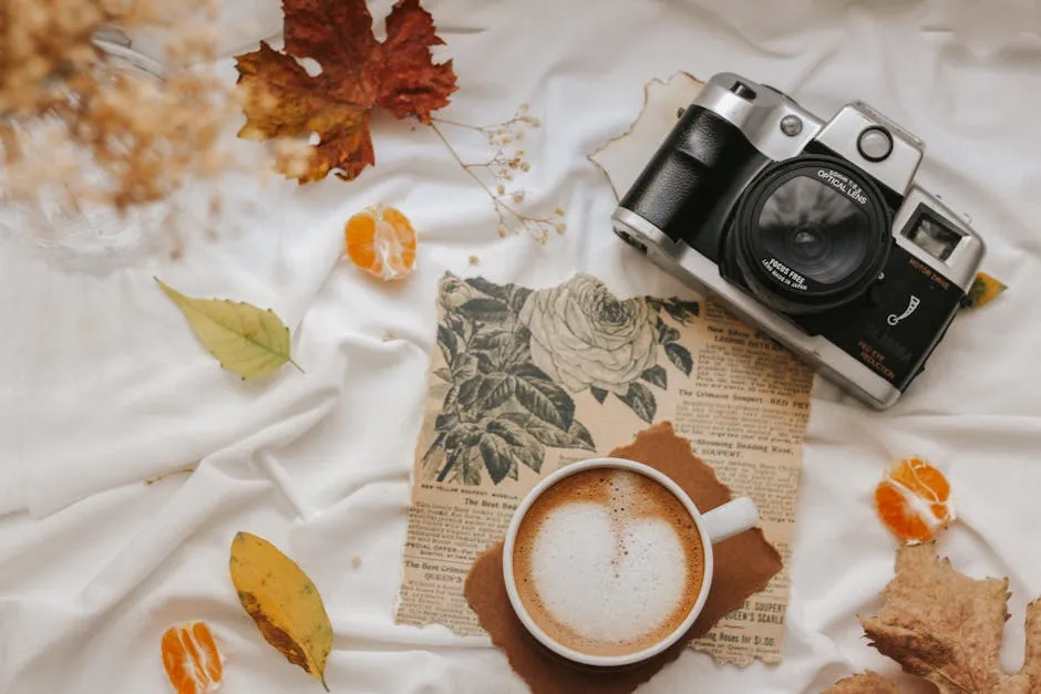 Flat lay of a vintage camera and coffee on an autumn-themed backdrop, evoking fall vibes.
