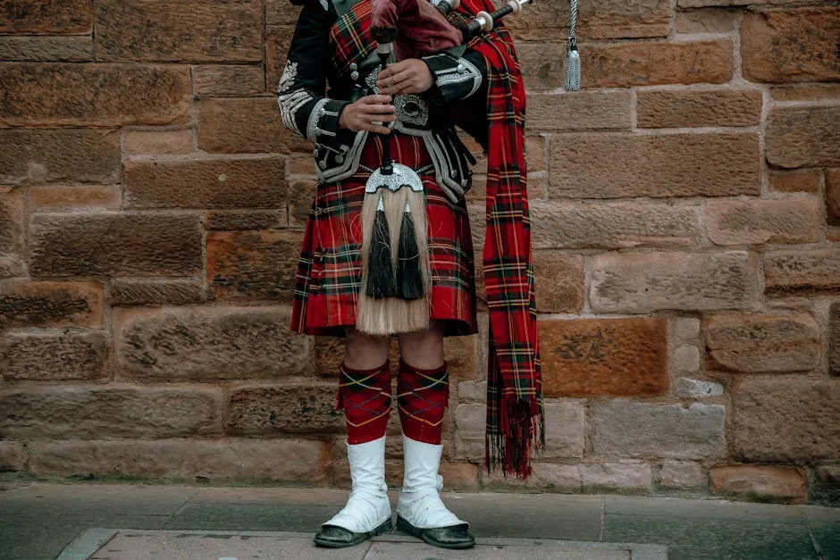 A Scottish bagpipe player in traditional attire with kilt against a stone wall.