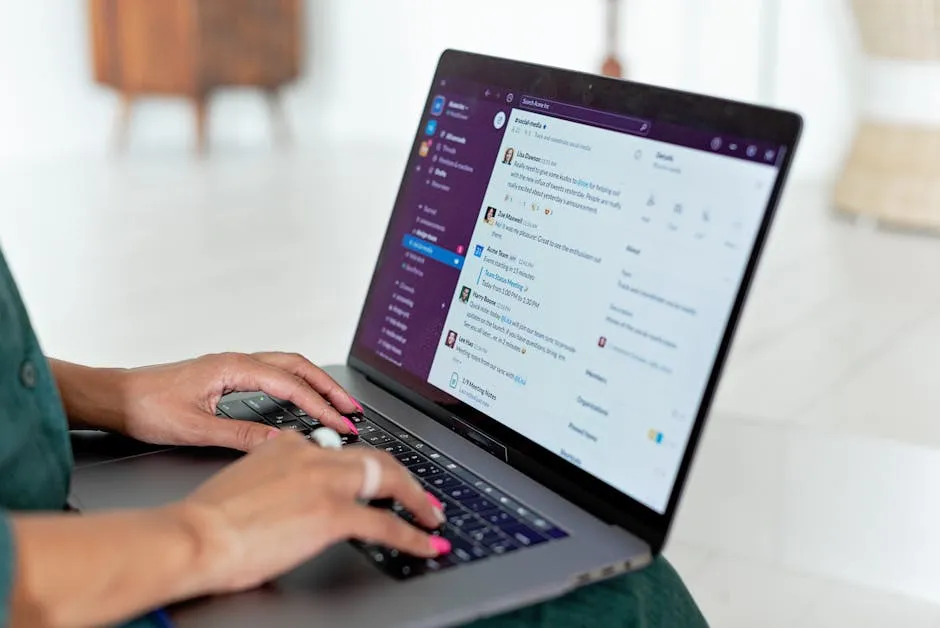 Woman typing on a laptop using a messaging app in a home setting, close-up of hands.