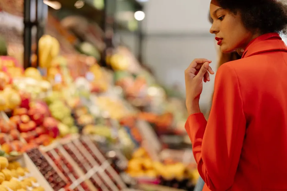 A fashionable woman in a red blazer selecting fresh fruits at a vibrant market.