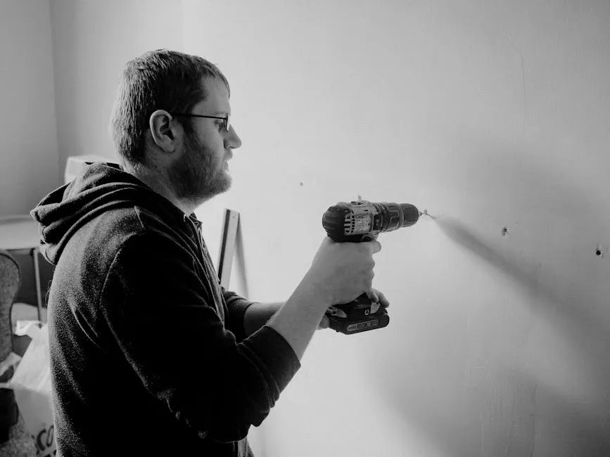 Man using a power drill to repair a wall inside a home. Black and white photo.